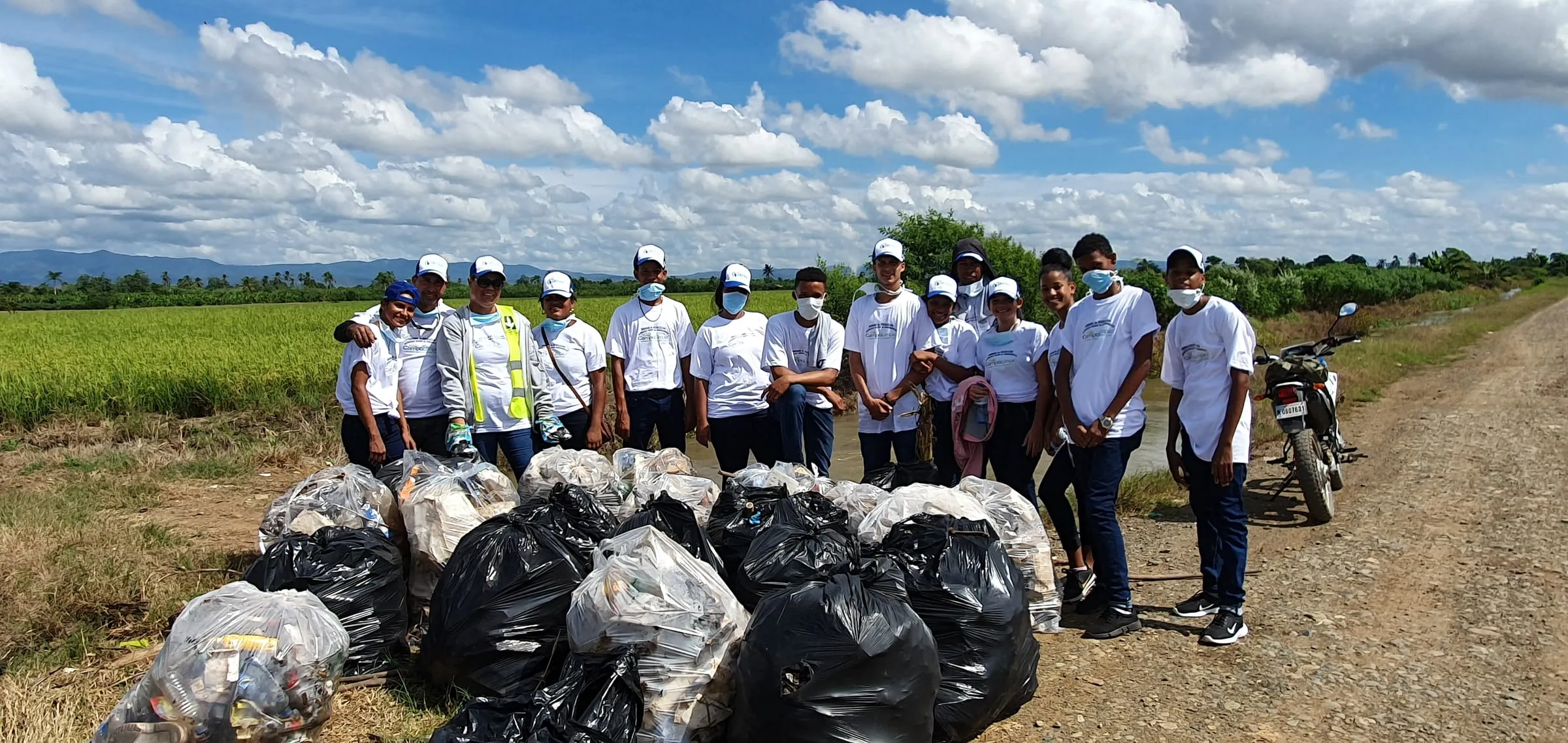 Grupo de voluntarios de Campo Limpio de pie junto al camino, detrás de una fila de sacos con los envases recogidos en los arrozales de Jima
