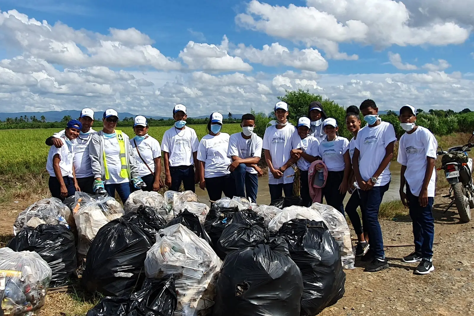 Grupo de voluntarios de Campo Limpio de pie junto al camino, detrás de una fila de sacos con los envases recogidos en los arrozales de Jima