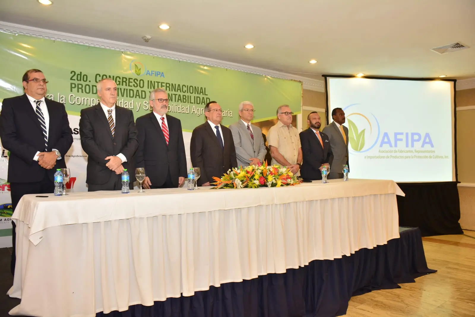 La mesa de honor del segundo congreso de AFIPA, de pie tras el estrado, ante el banner verde del evento y la proyección del logo de la asociación
