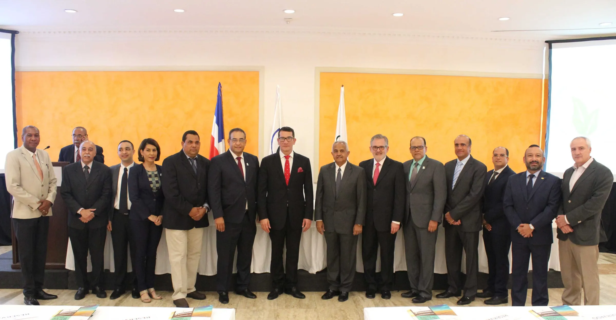 Directivos e invitados del tercer congreso posan de pie en fila delante de la mesa de honor y la bandera dominicana